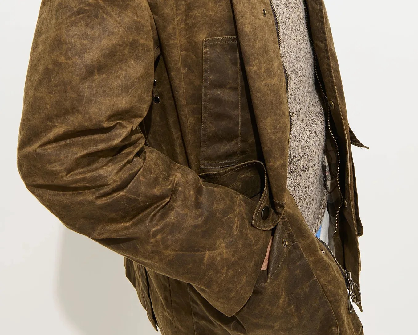 Brown waxed cotton jacket with snap button and zipper closure worn over a gray knit sweater.