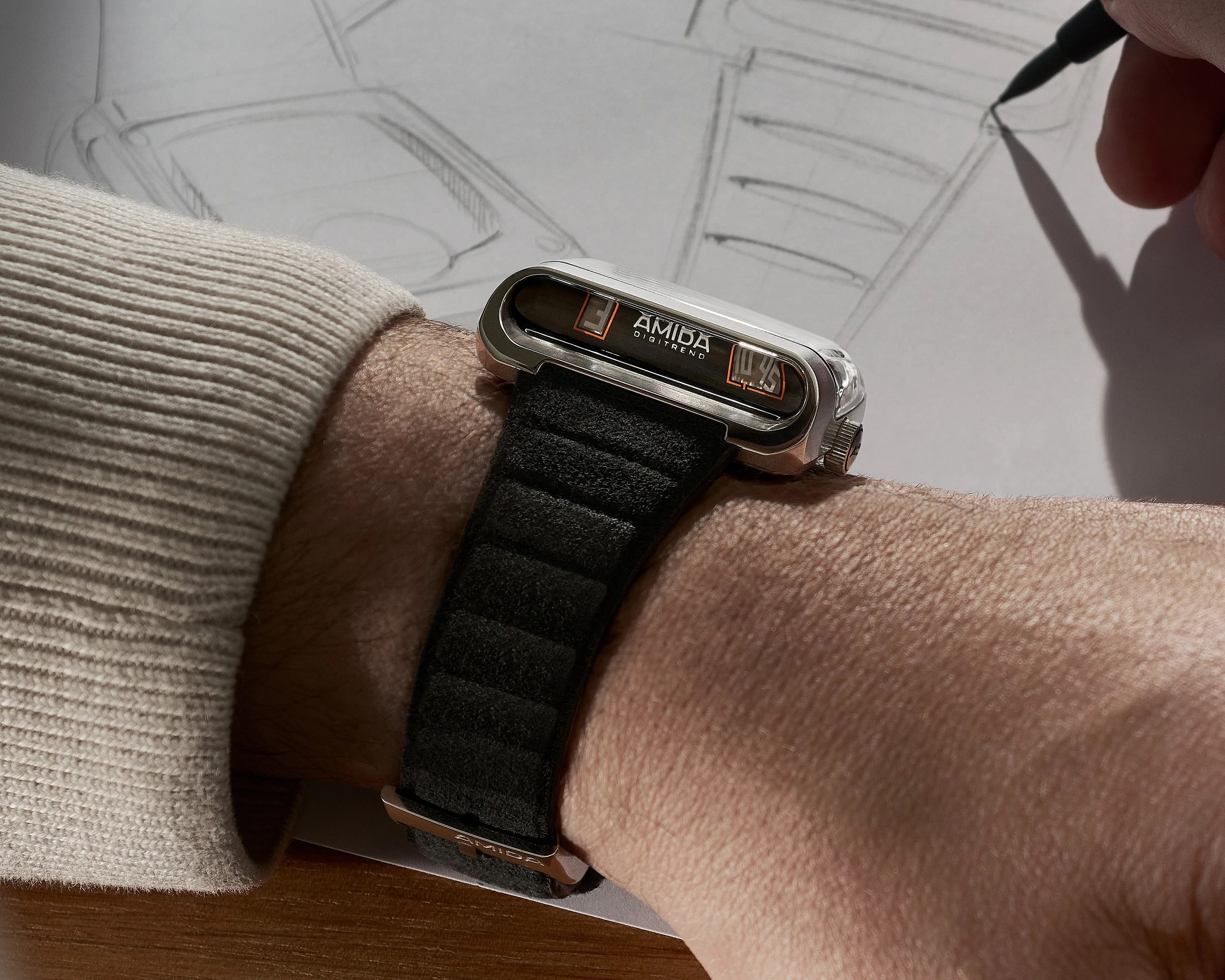 Silver digital wristwatch with black padded strap worn on a wrist over a beige ribbed sleeve.