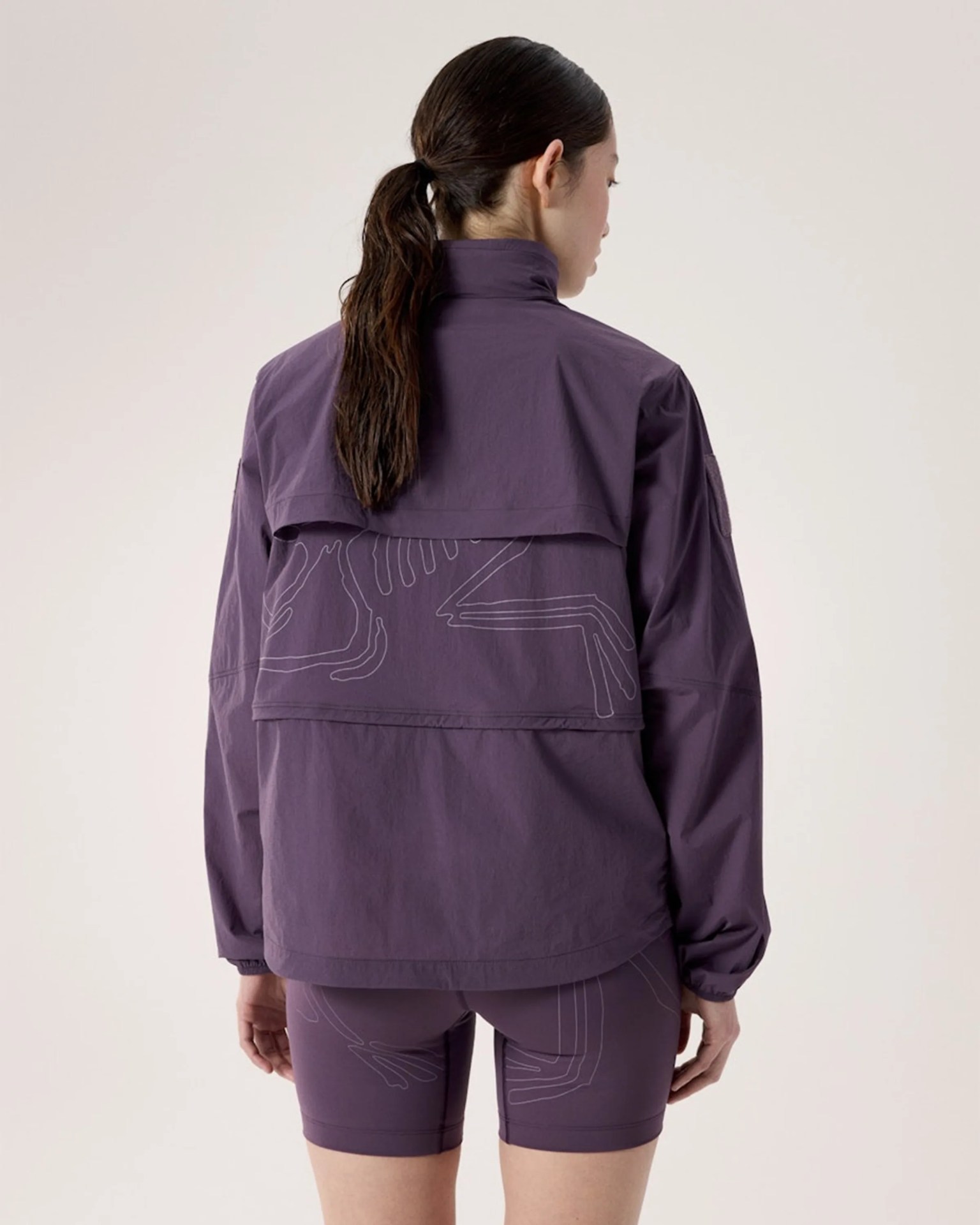 Woman wearing a purple jacket and matching shorts with abstract line designs, viewed from the back.