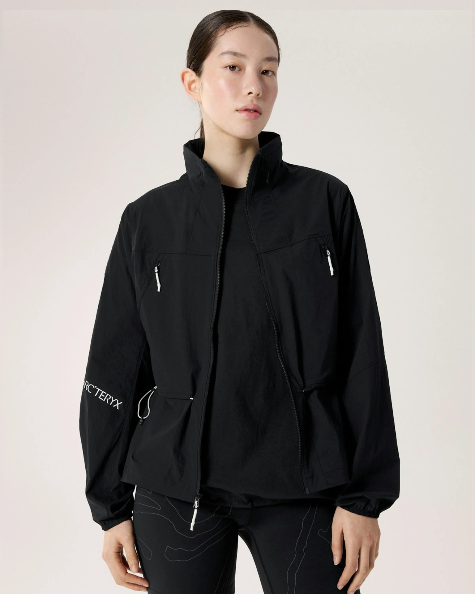 Black zip-up jacket with high collar and white zipper pulls worn by a person.