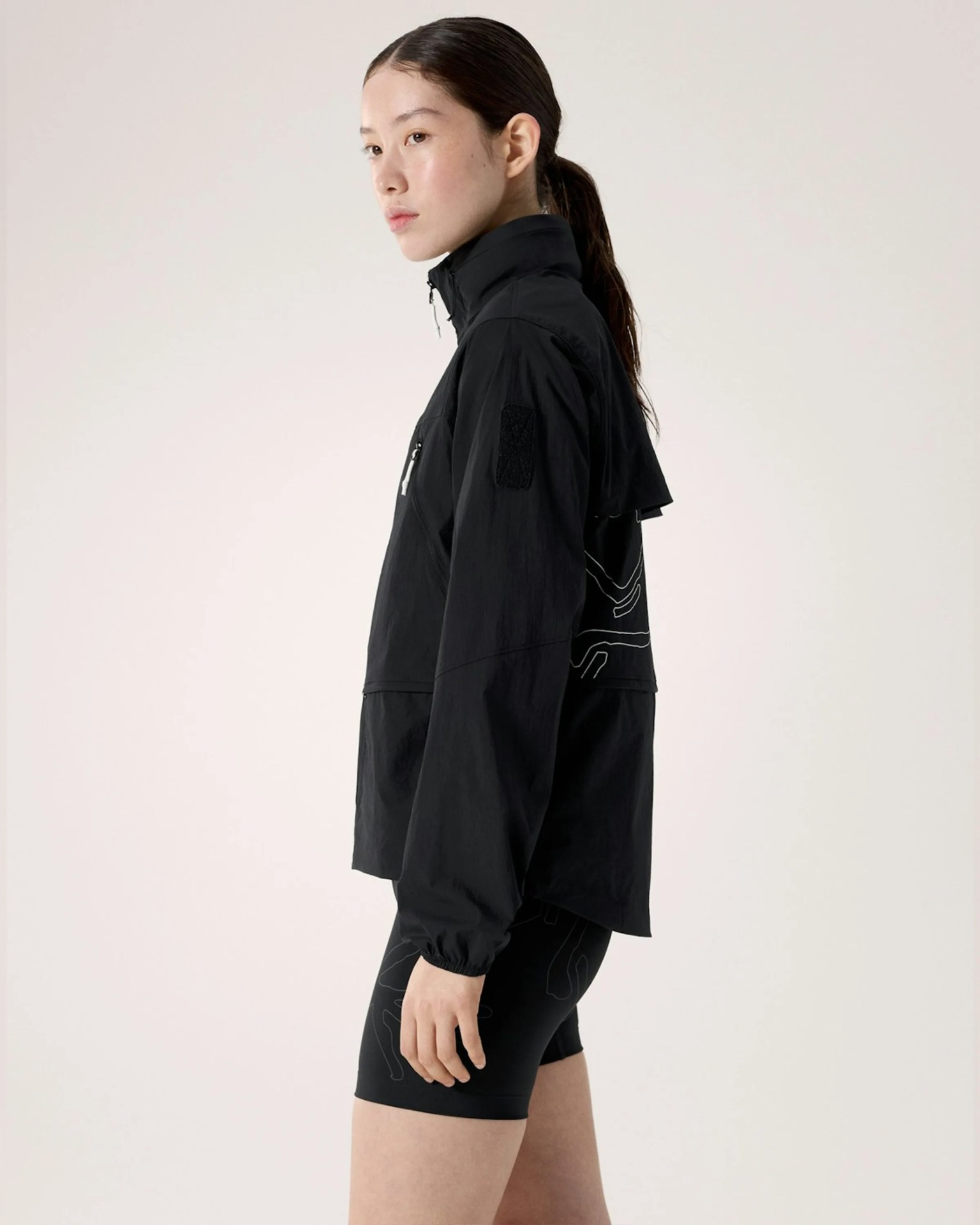 Black lightweight jacket with high collar and zippered chest pocket worn by a person in profile.