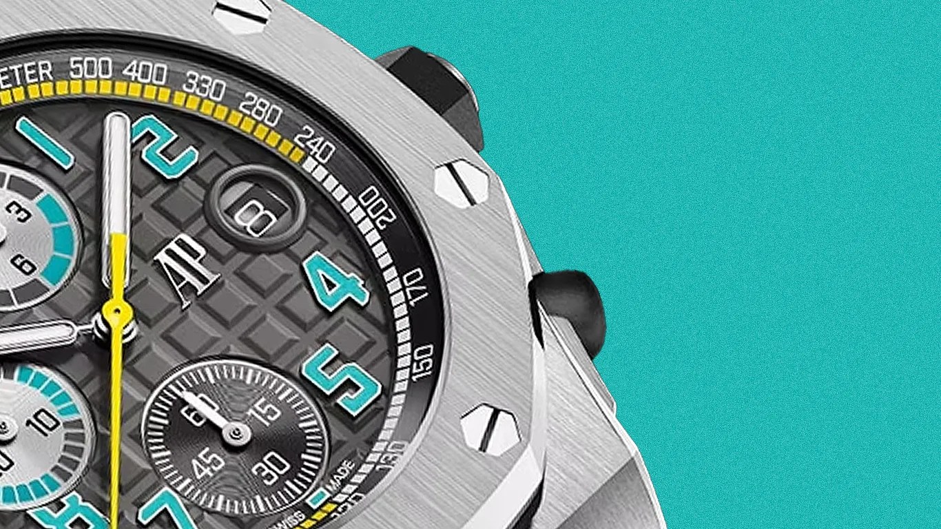 Close-up of a silver chronograph watch with turquoise numerals, yellow second hand, and textured black dial.