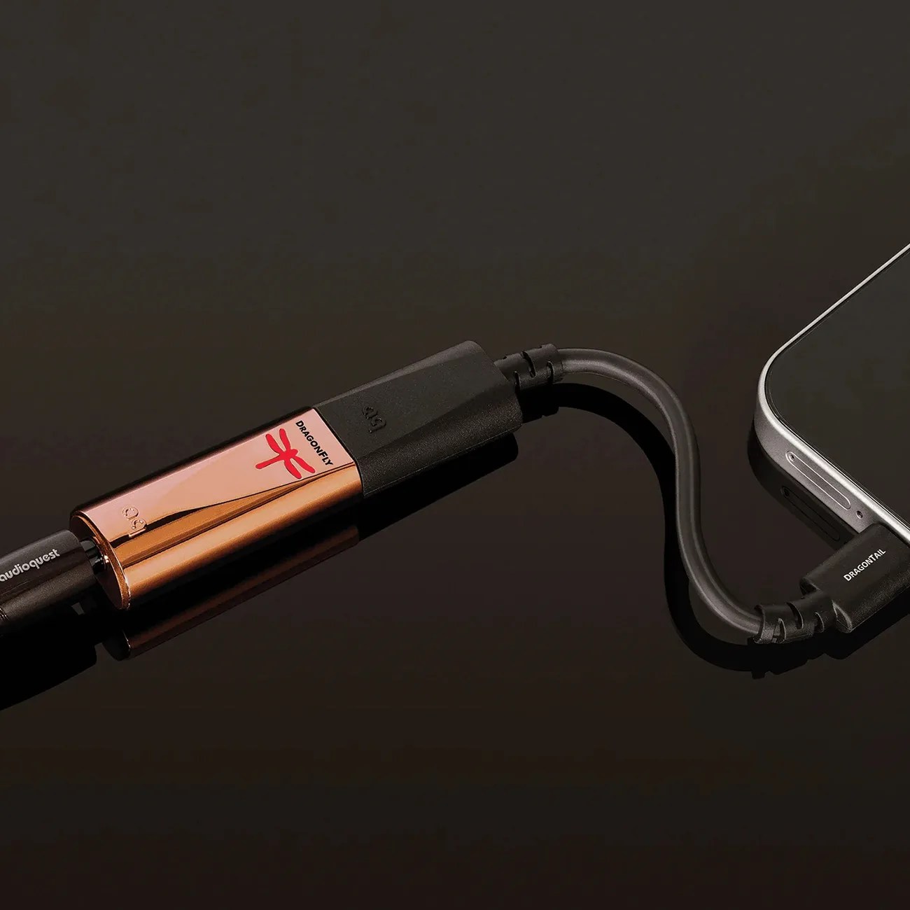 Copper-colored DragonFly USB digital-to-analog converter connected to a smartphone via a short black cable labeled "DRAGONTAIL.