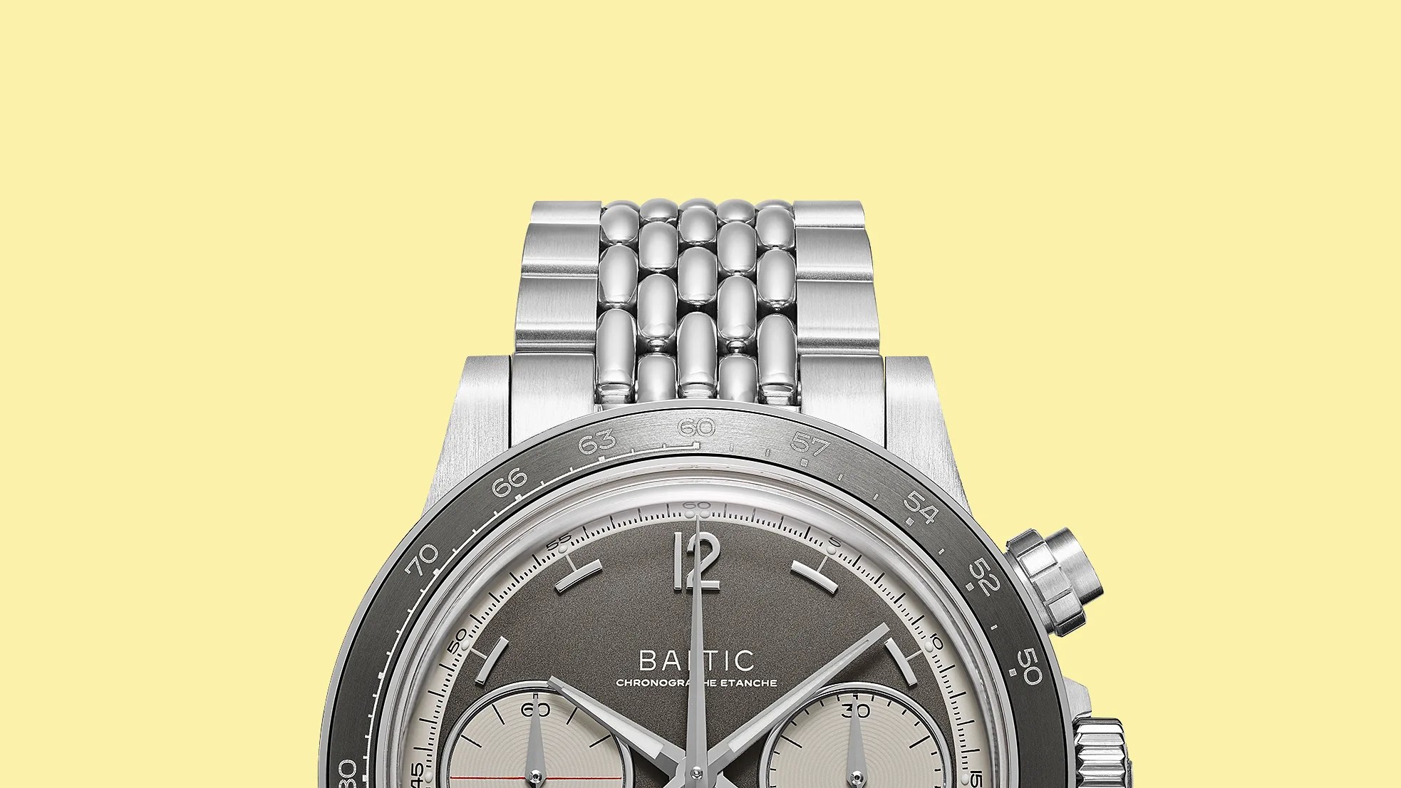 Close-up of a silver Baltic chronograph watch with a gray dial and a polished metal bracelet against a yellow background.