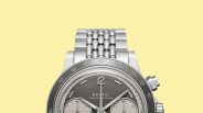 Close-up of a silver Baltic chronograph watch with a gray dial and a polished metal bracelet against a yellow background.
