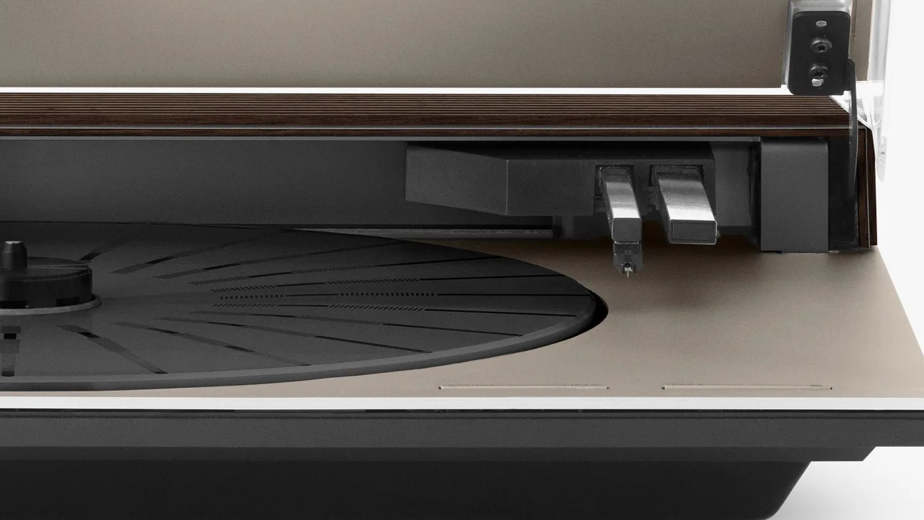 Close-up of a modern turntable's black platter and tonearm assembly on a beige base with a transparent dust cover.