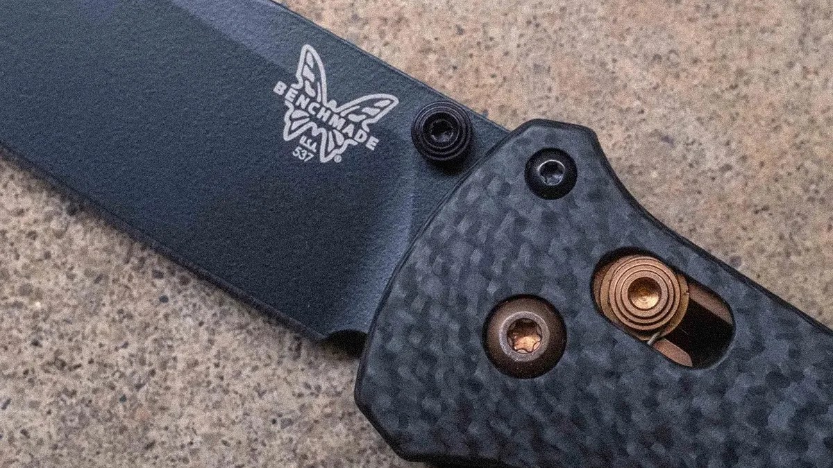 Close-up of a black Benchmade folding knife blade and textured carbon fiber handle with visible screws and spring mechanism.