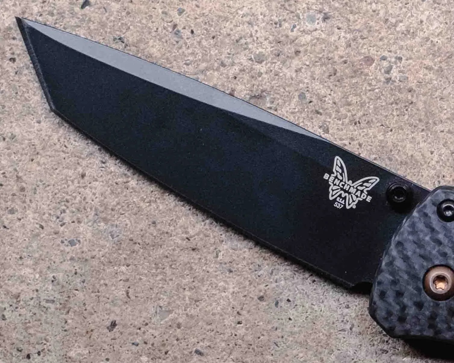 Black Benchmade folding knife with carbon fiber handle on a concrete surface.