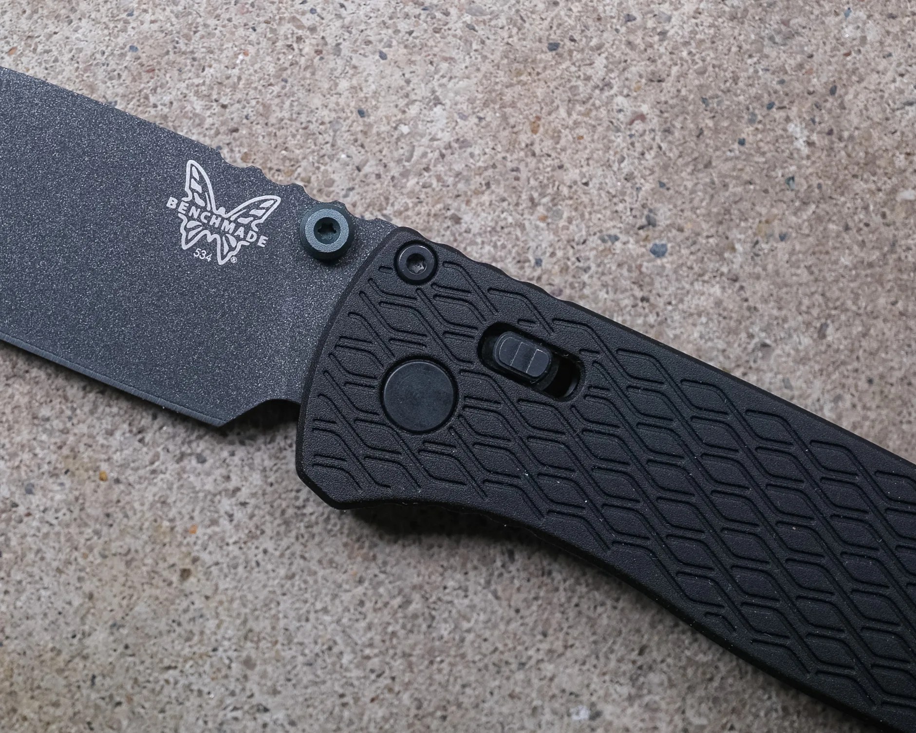 Black Benchmade folding knife with textured handle and partially serrated blade on a concrete surface.