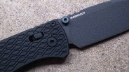 Black folding knife with textured handle and "MAGNACUT" printed on the blade, resting on a rough surface.
