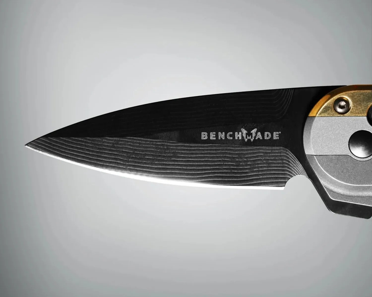 Close-up of a black Benchmade knife blade with a textured pattern and part of a silver and gold handle.