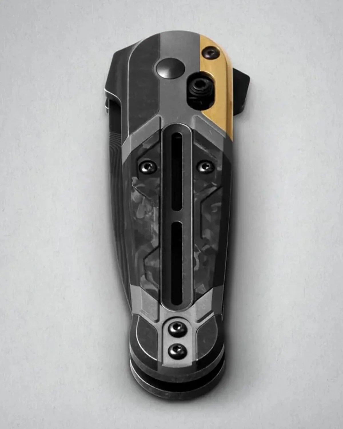 Folded black and gray folding knife with a gold accent and visible screws on a light gray surface.