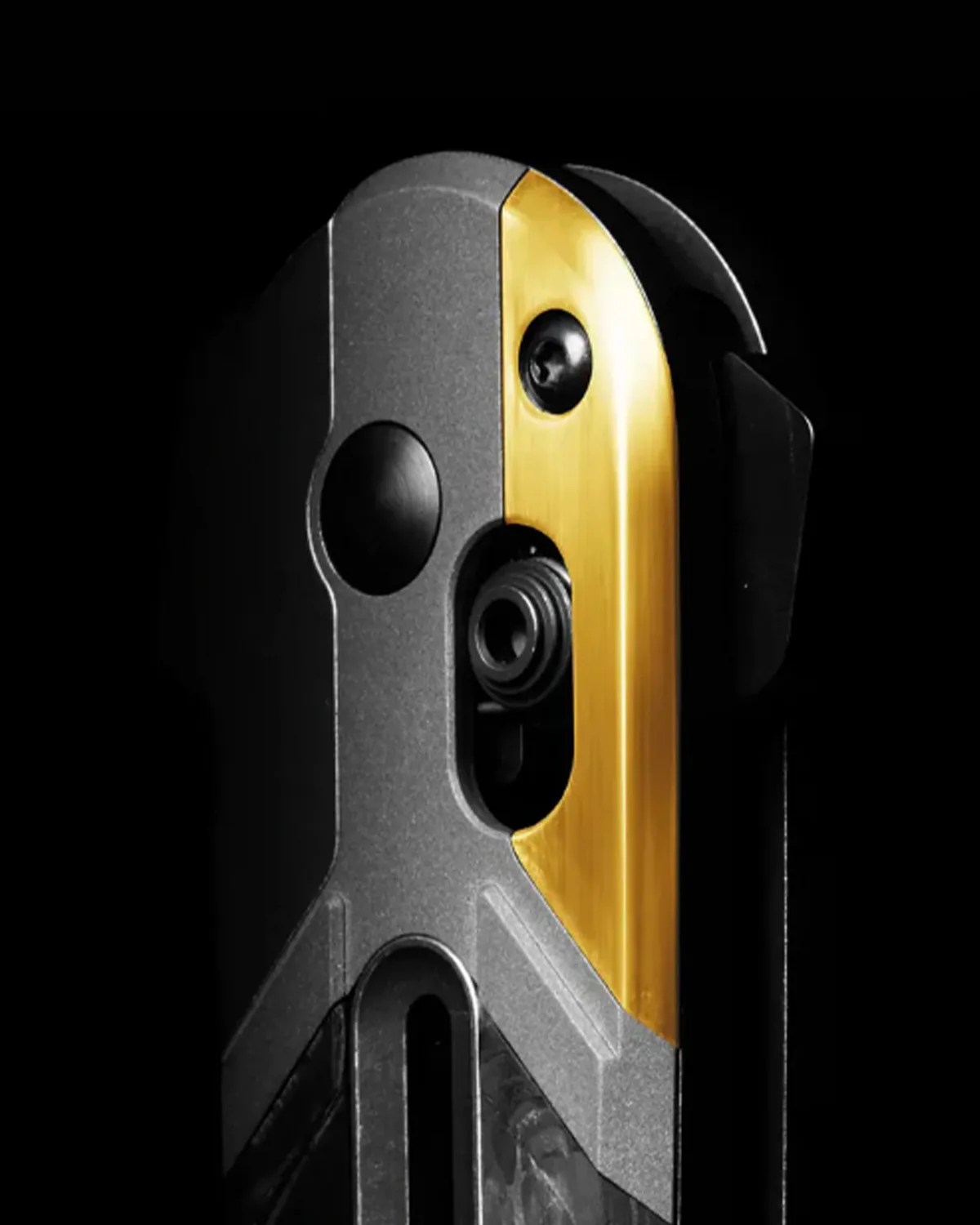 Close-up of a black and gold metallic device with a circular button and a small lens or camera on a black background.