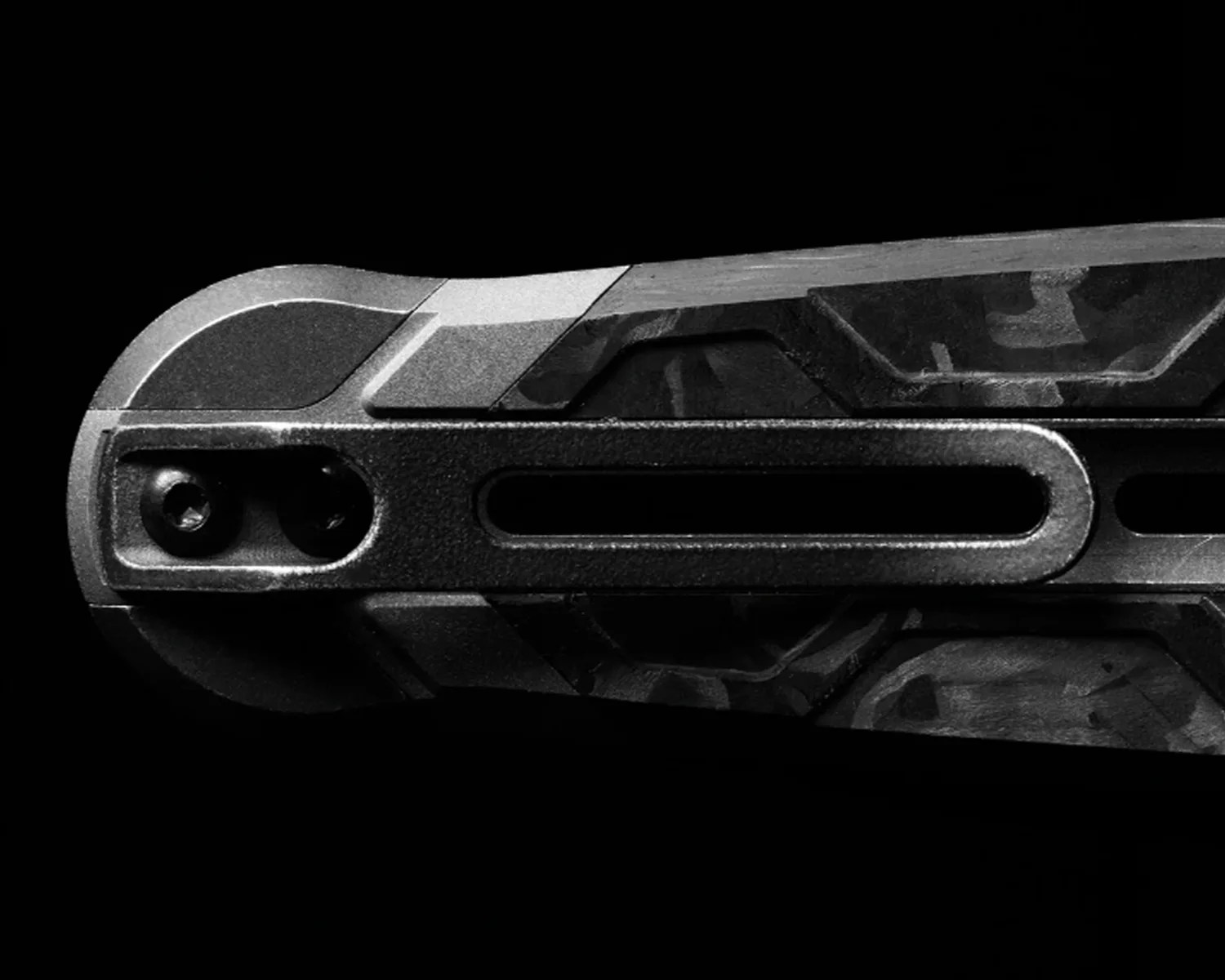 Close-up of a black and gray textured metal object with screws and a long vertical slot against a black background.