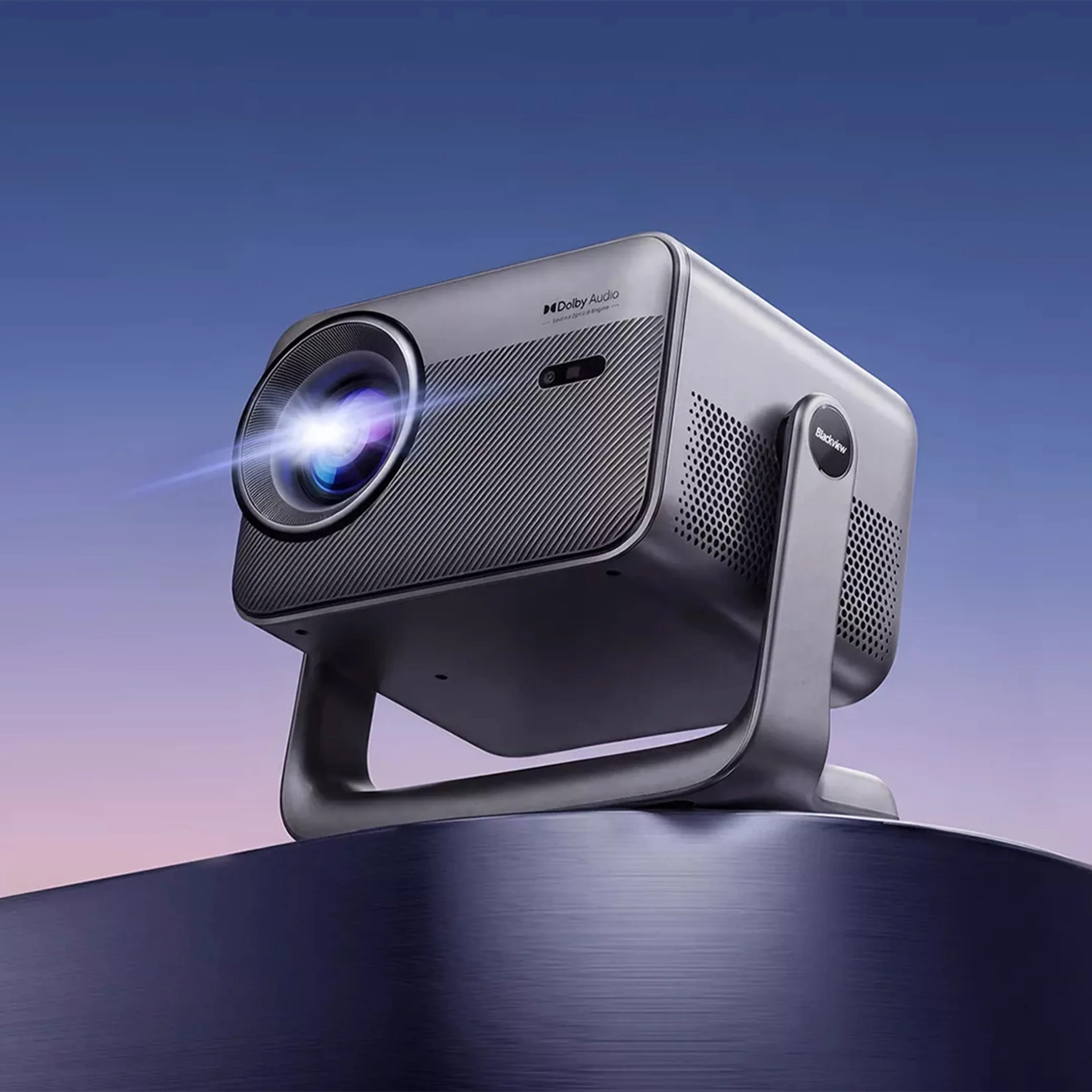 Blackview projector with Dolby Audio logo and lens emitting light, mounted on a dark metallic surface.