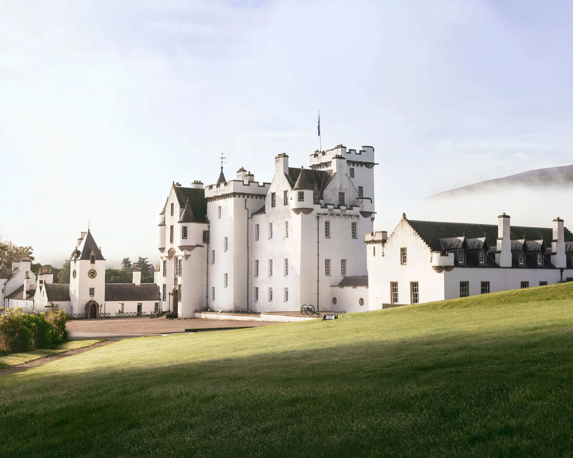 Large white castle with multiple chimneys and turrets on a grassy hill under a clear sky.
