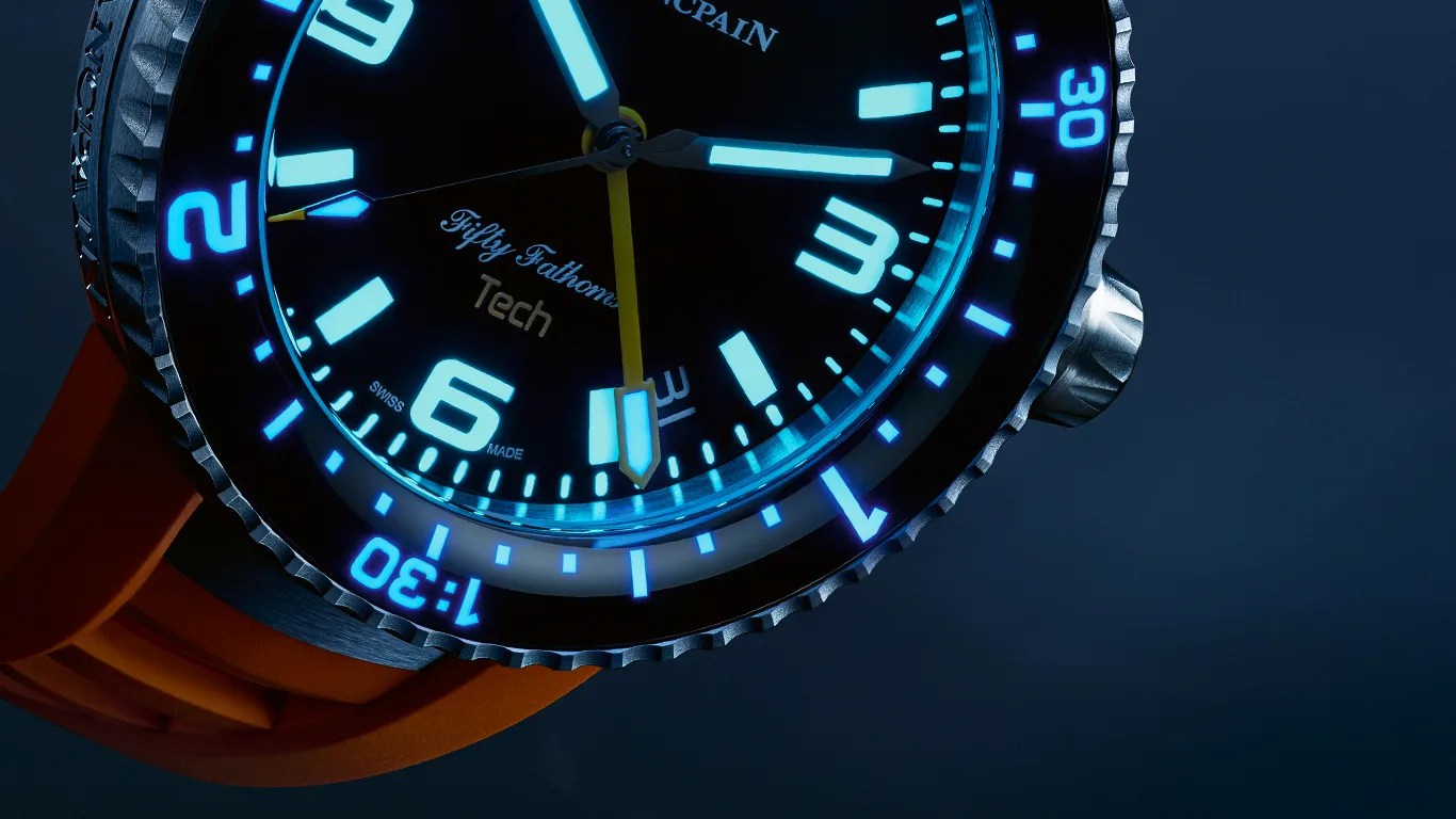 Close-up of a Blancpain Fifty Fathoms Tech dive watch with glowing blue markers and an orange strap.