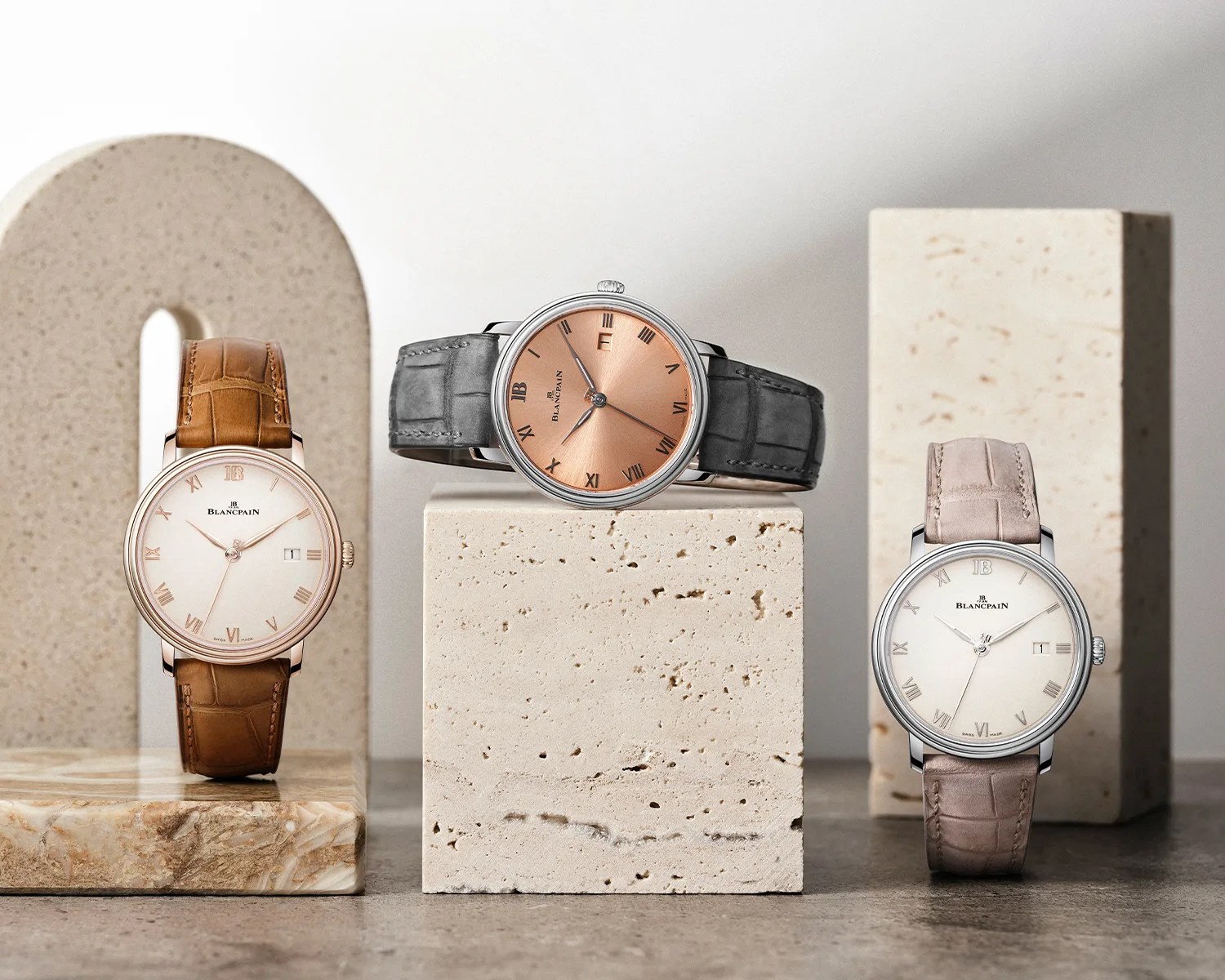 Three Blancpain wristwatches with Roman numeral dials and leather straps displayed on beige stone blocks.