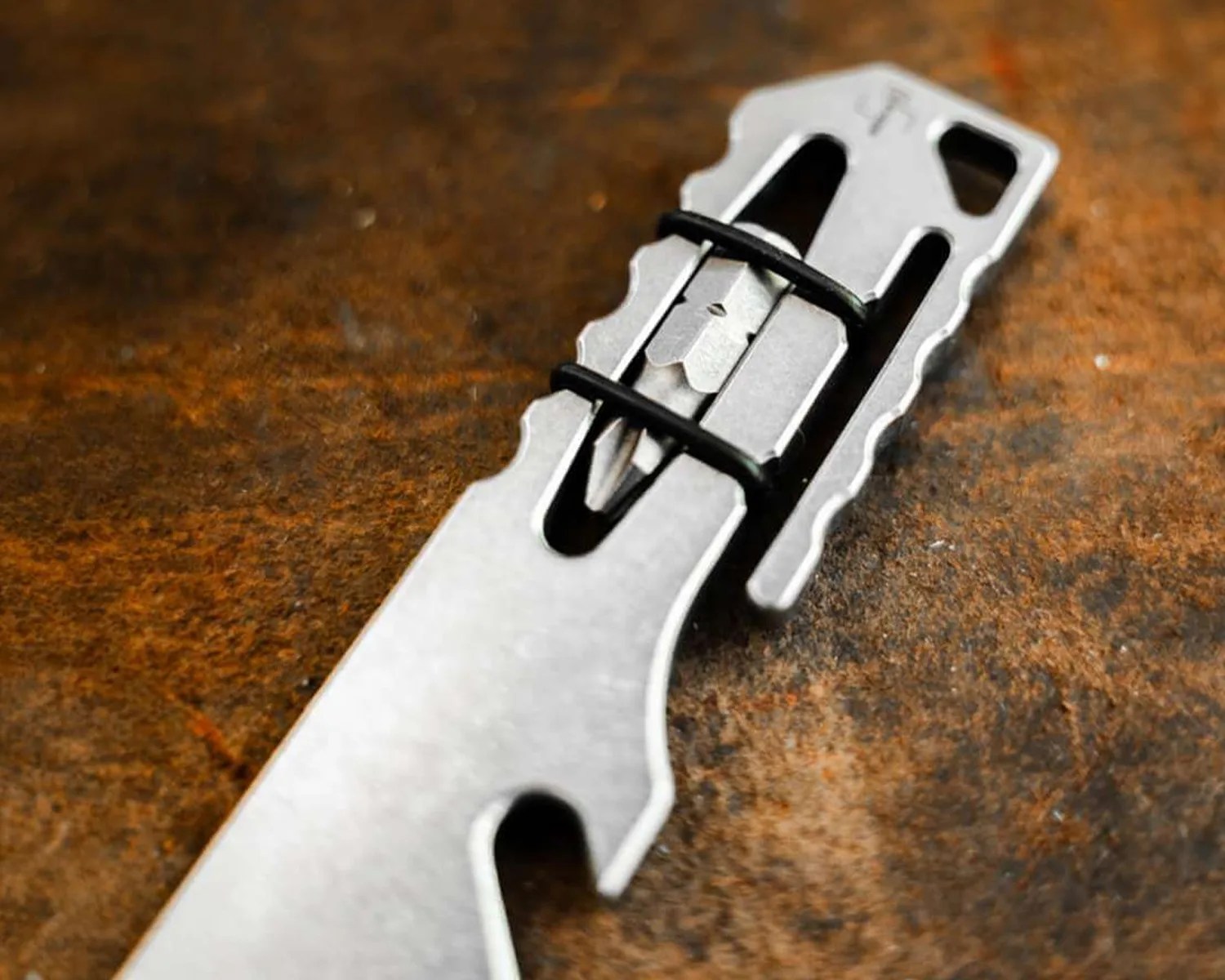 Close-up of a silver multi-tool with black rubber bands securing a small blade on a rusty brown surface.