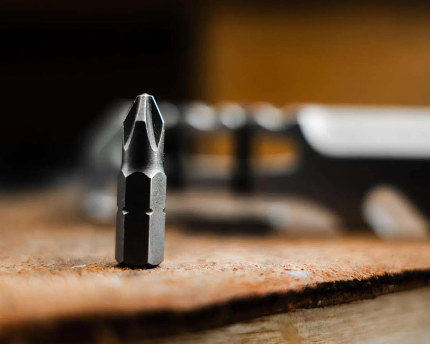 Close-up of a metal Phillips screwdriver bit standing upright on a wooden surface.