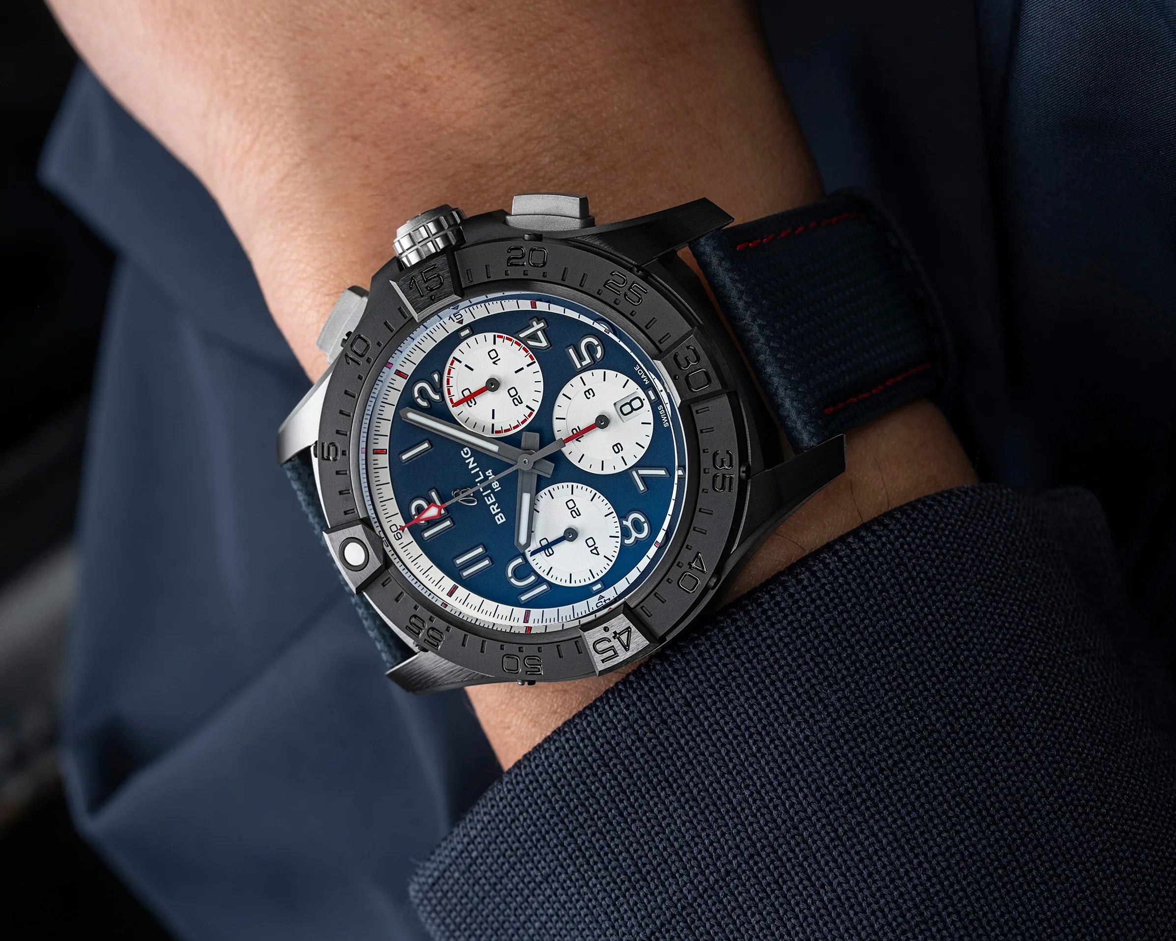 Black and silver Breitling chronograph watch with blue dial and white subdials on a wrist with blue fabric strap.