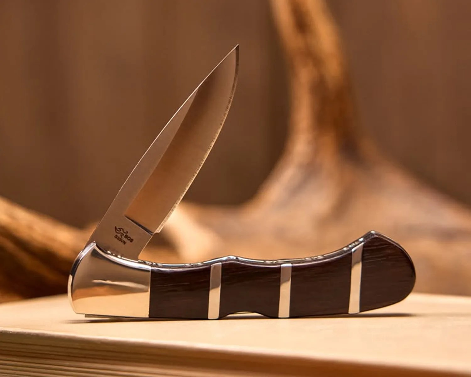 Folding pocket knife with polished steel blade and dark wood handle with metal accents on a wooden surface.