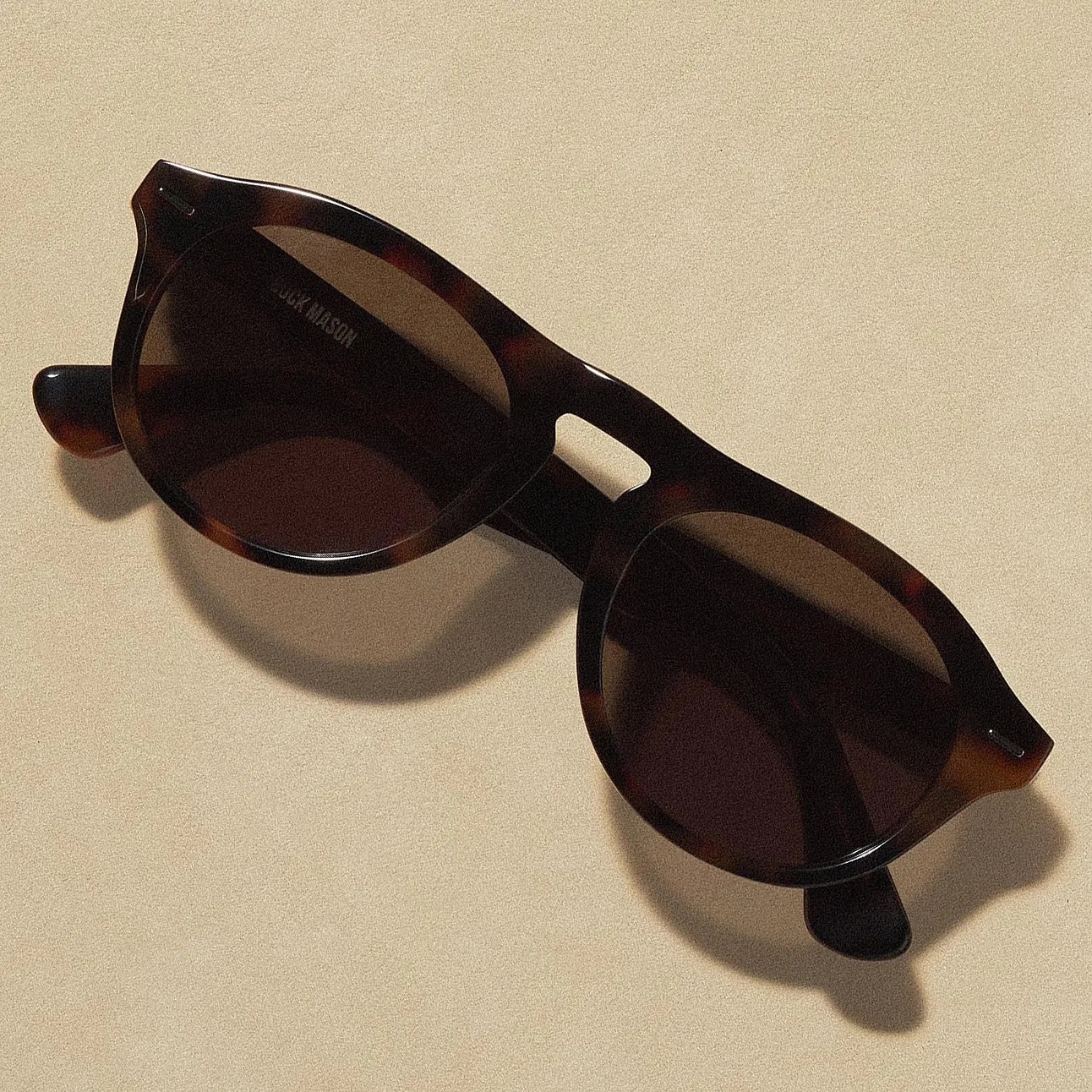 Tortoiseshell round sunglasses with dark lenses on a beige surface.