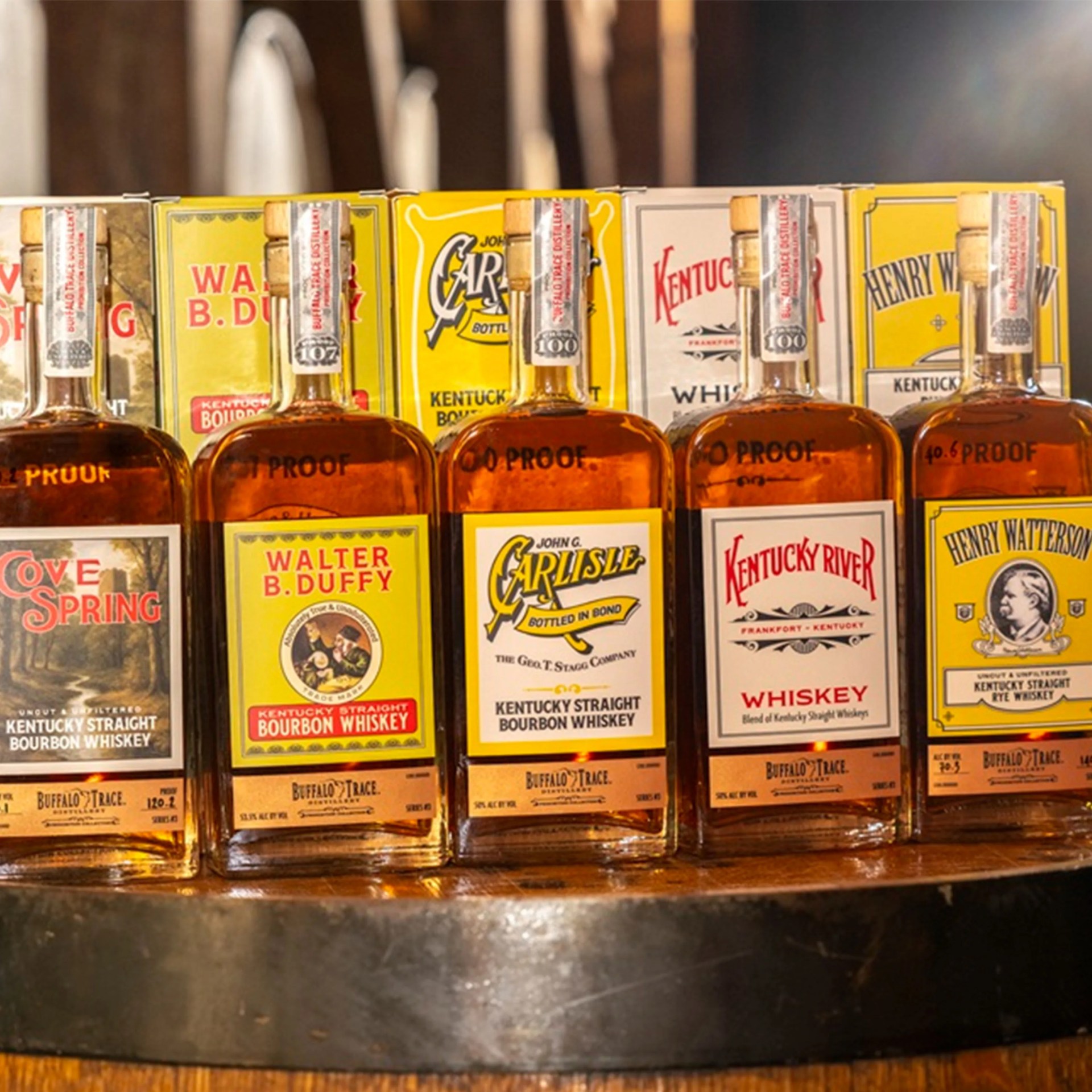 Five bottles of Kentucky straight bourbon whiskey with colorful labels and wooden corks lined up on a wooden surface.