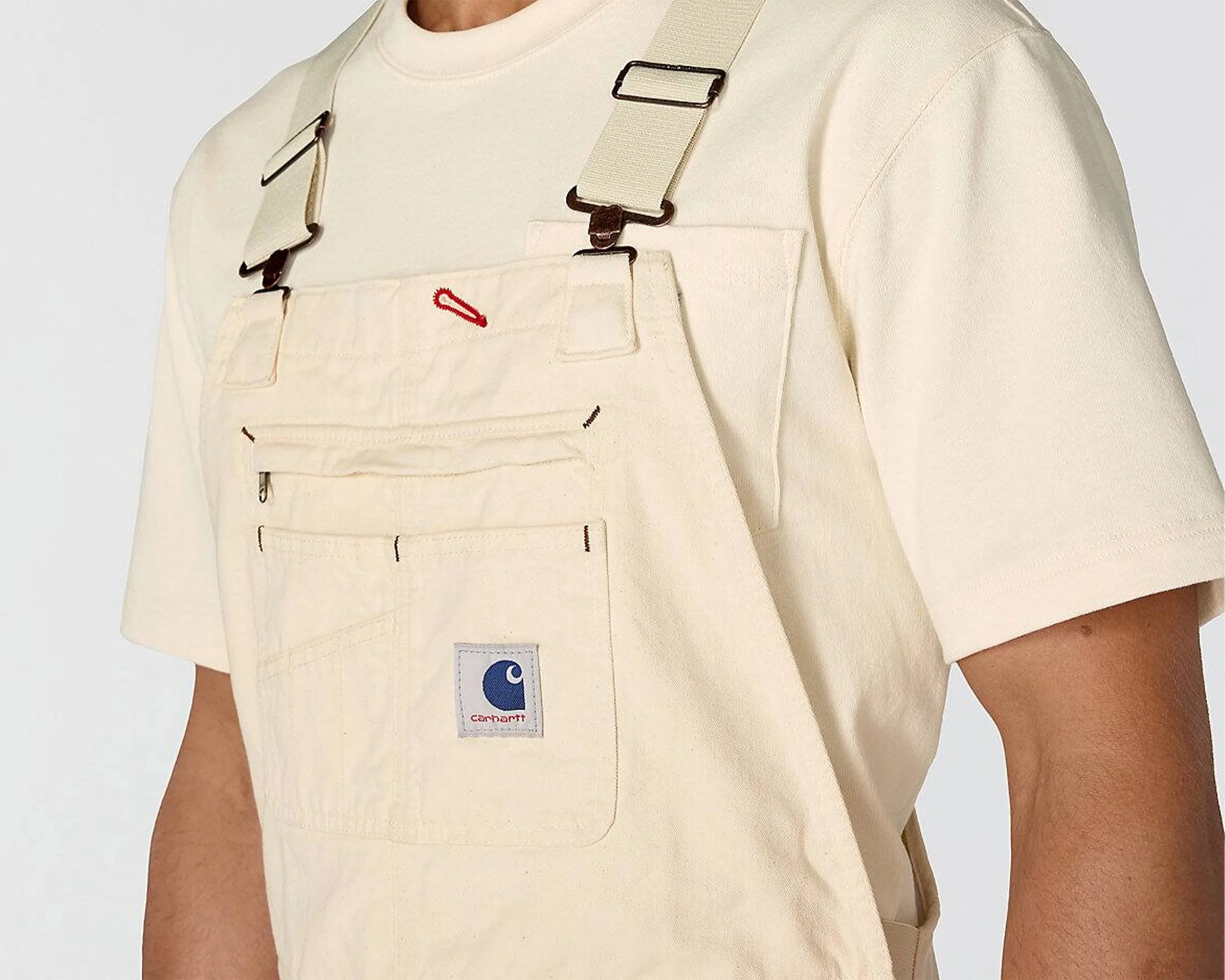 Beige Carhartt overalls with adjustable straps worn over a matching beige T-shirt.