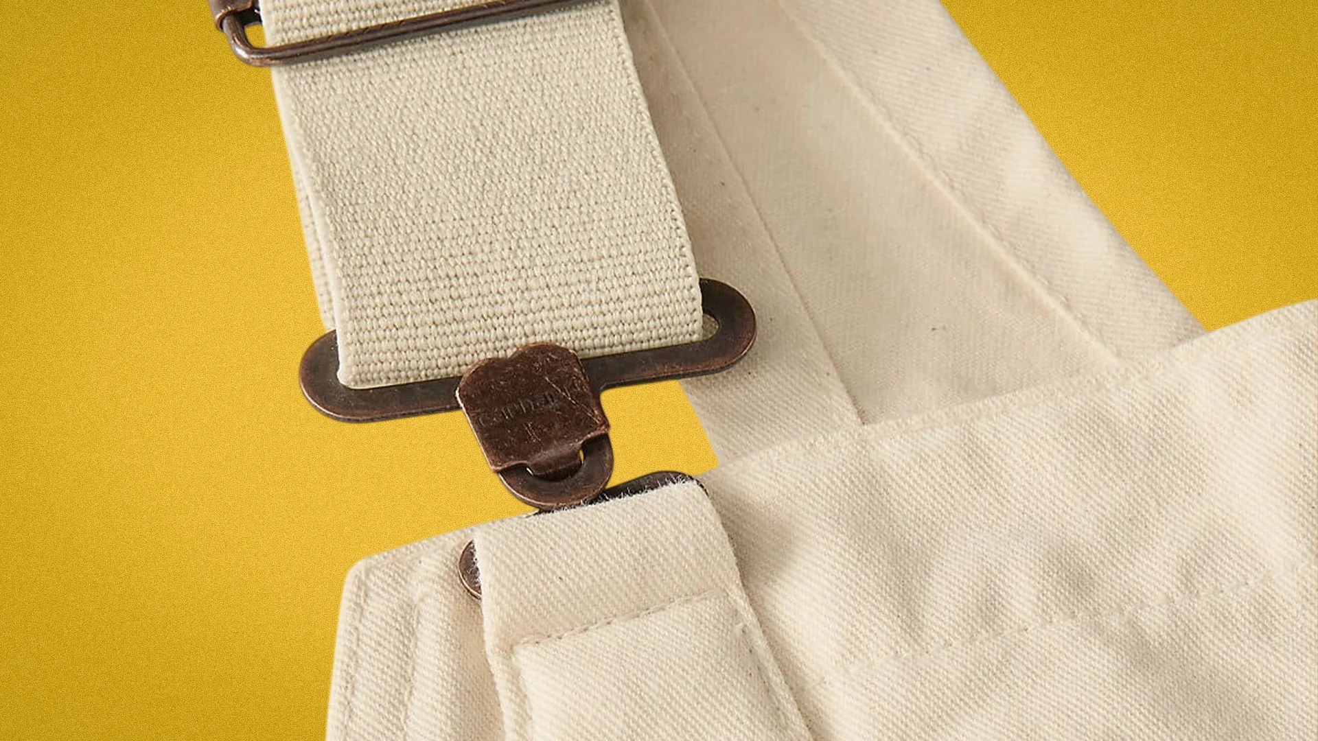 Close-up of beige canvas strap with metal clip attached to beige fabric.