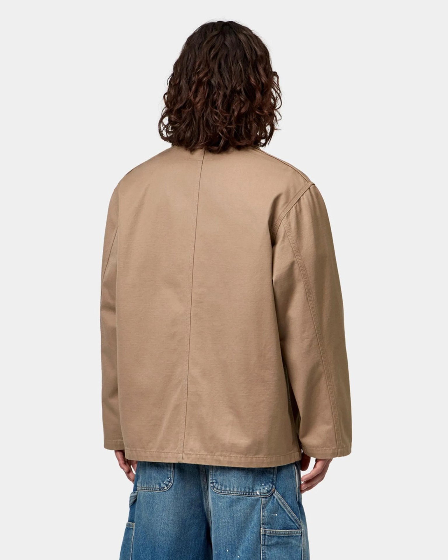 Beige long-sleeve jacket with visible seam down the back worn over blue denim pants.