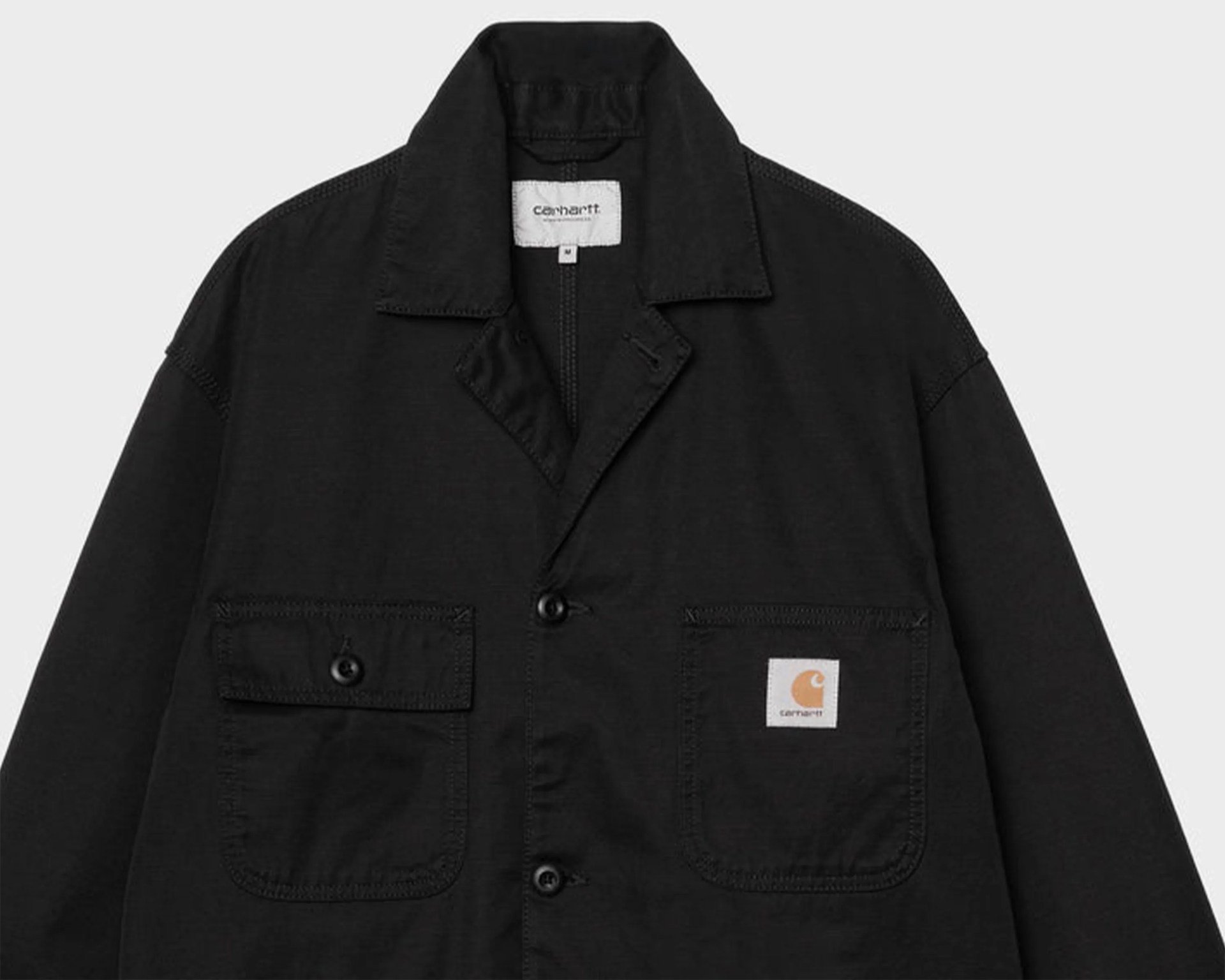 Black Carhartt jacket with buttoned front and two chest pockets, one featuring a Carhartt logo patch.