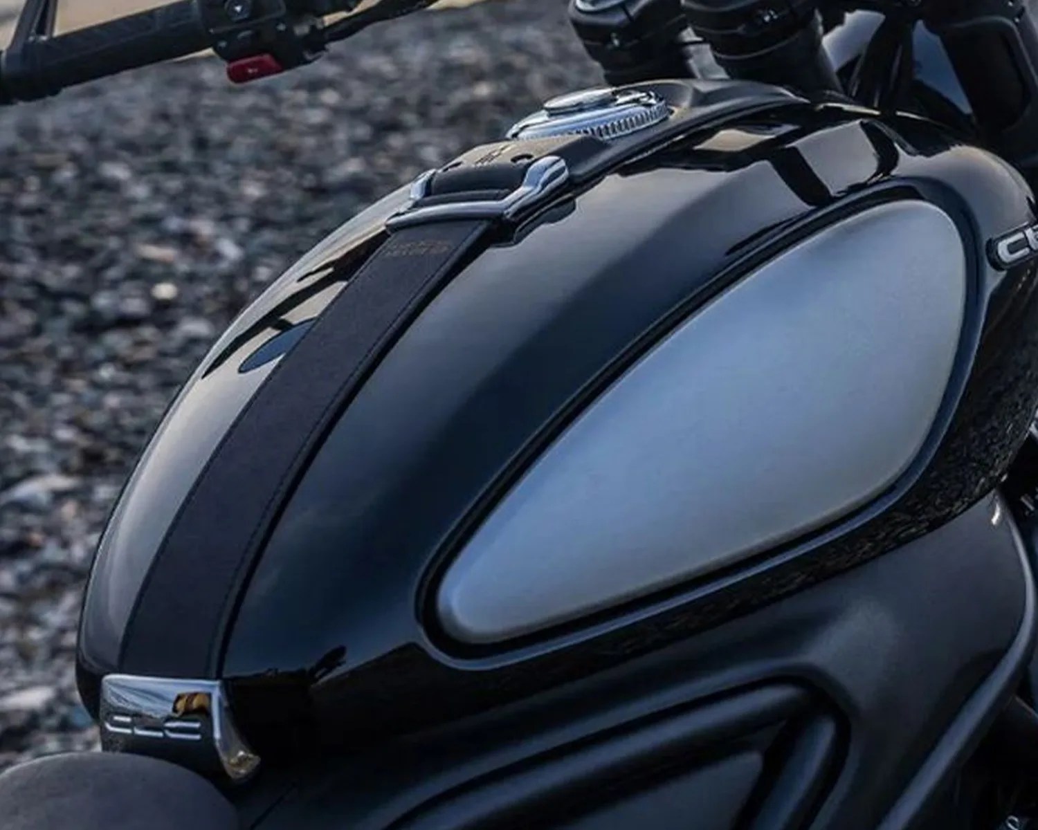 Glossy black motorcycle fuel tank with a matte gray side panel and a black strap across the top.