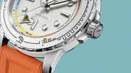 Close-up of a silver diver's watch with a white dial, orange rubber strap, and detailed bezel markings.