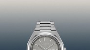 Close-up of a silver Citizen wristwatch with a metal link band and day-date display on a gradient gray background.