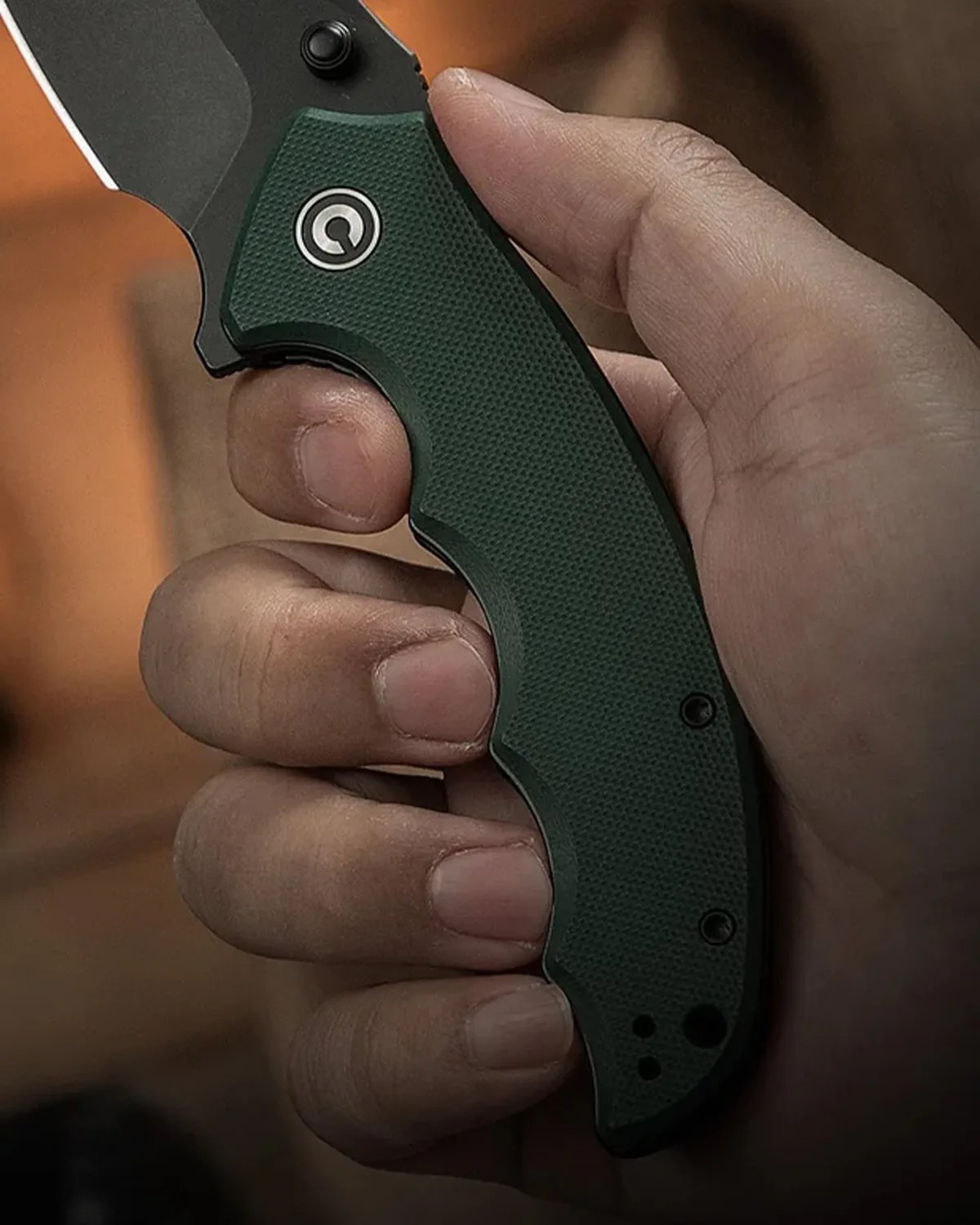 Hand holding a folding knife with a textured dark green handle and a partially visible black blade.