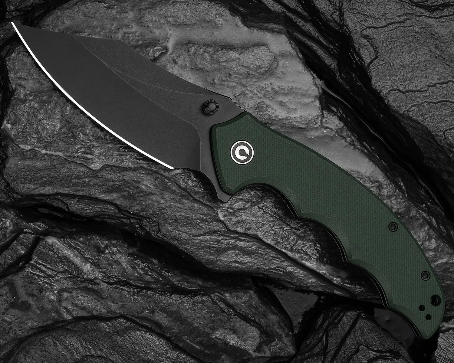 Folding knife with a black blade and dark green textured handle on a dark rocky surface.