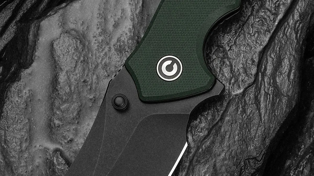Close-up of a black folding knife blade with a green textured handle featuring a circular logo.