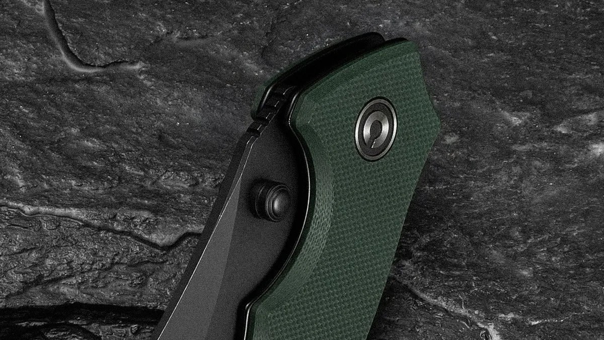 Folding knife with a textured green handle and black blade resting on a dark stone surface.