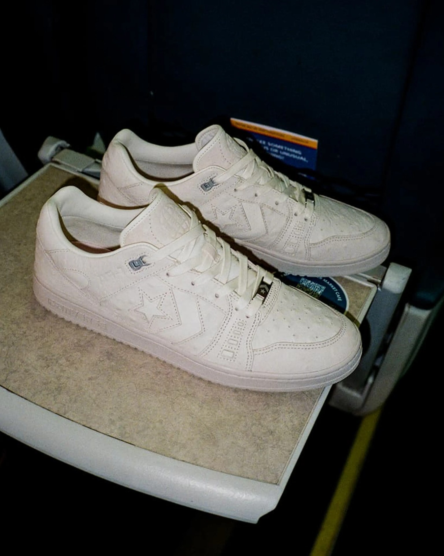 Off-white leather Converse sneakers with star logo on side placed on a beige tray table.