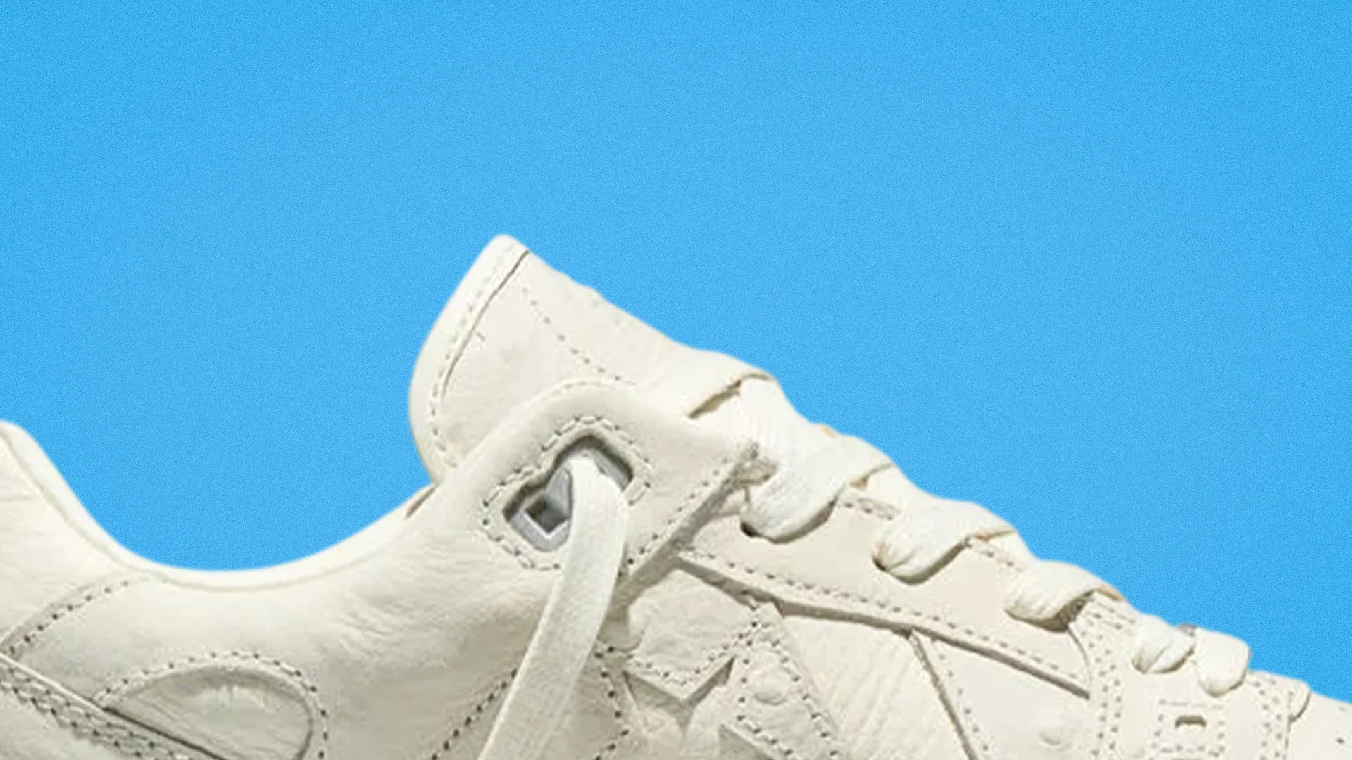 Close-up of a white leather sneaker with white laces against a blue background.