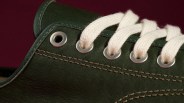 Close-up of dark green leather shoe with white laces threaded through metal eyelets.