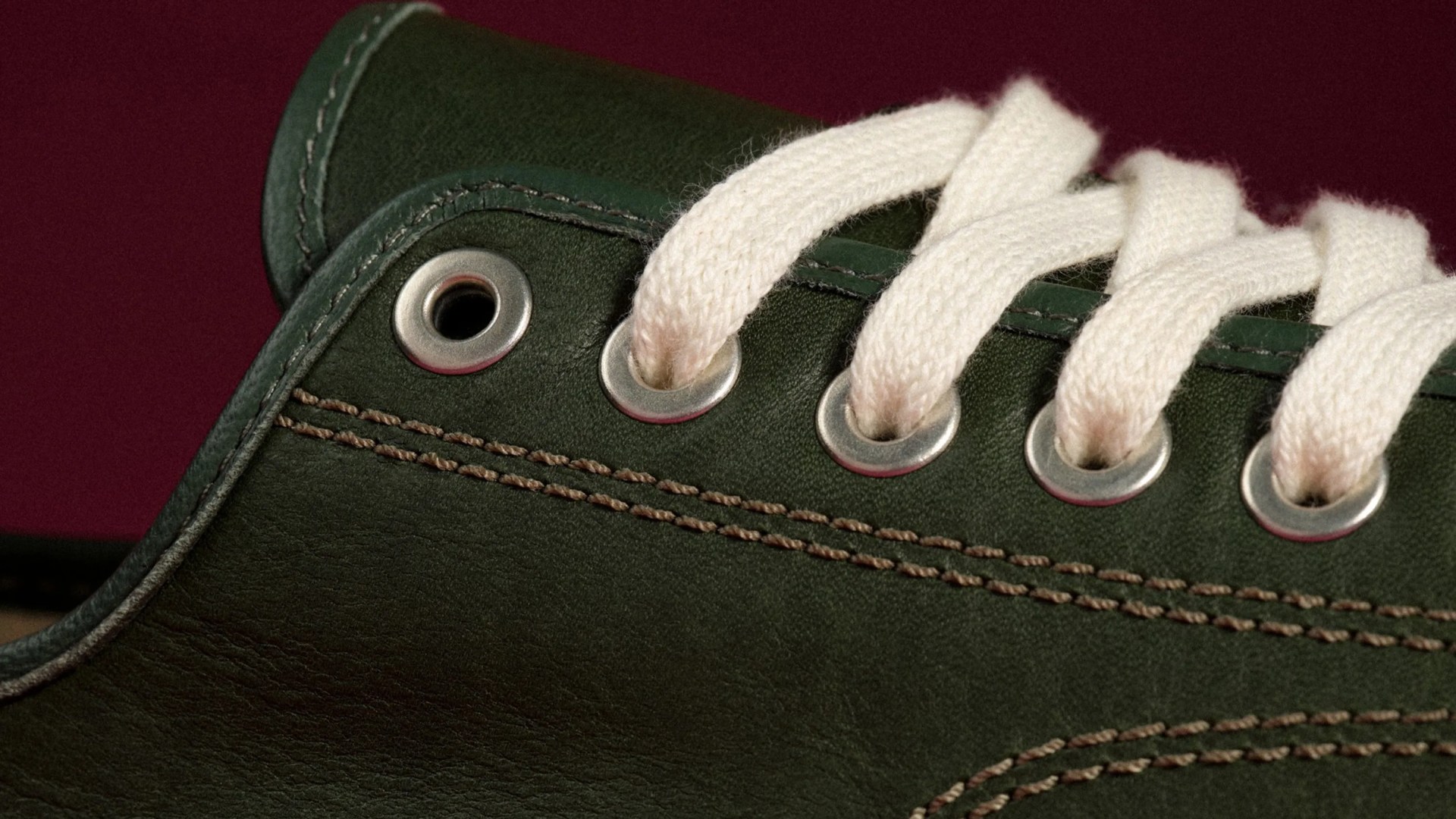 Close-up of dark green leather shoe with white laces threaded through metal eyelets.
