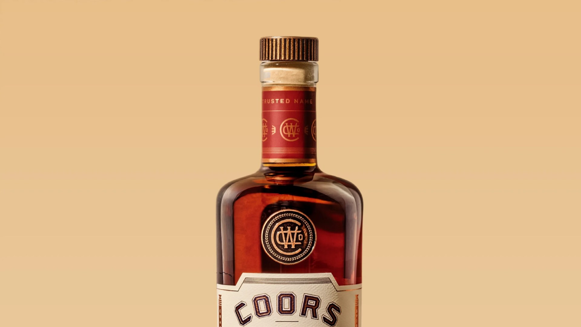 Close-up of the top half of a Coors whiskey bottle with a wooden cap and red label on a beige background.