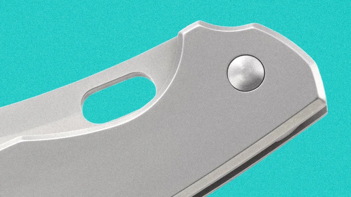 Close-up of a silver folding knife handle with a circular pivot and an oval cutout on a turquoise background.