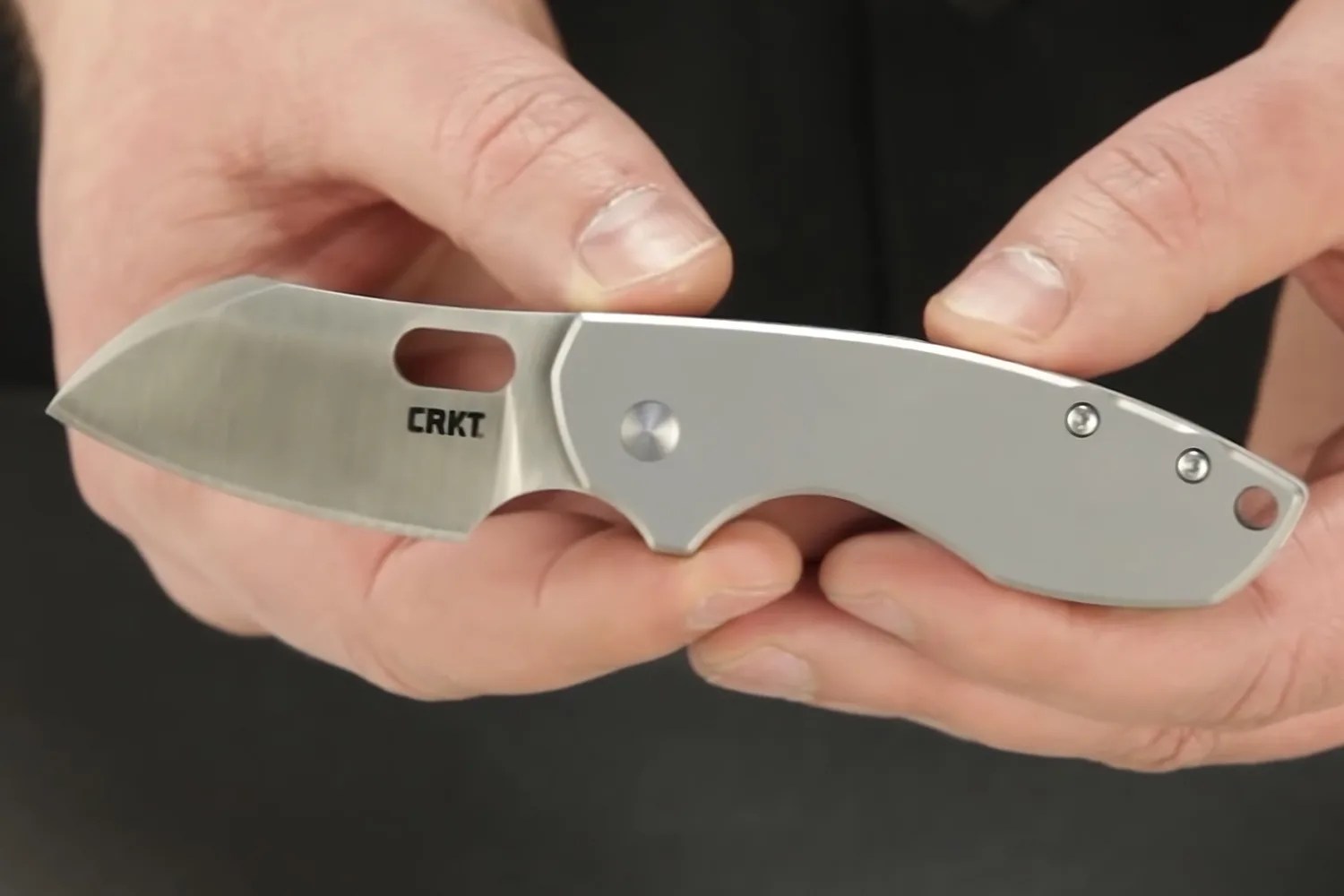 Silver folding knife with a short blade and "CRKT" logo held in two hands.