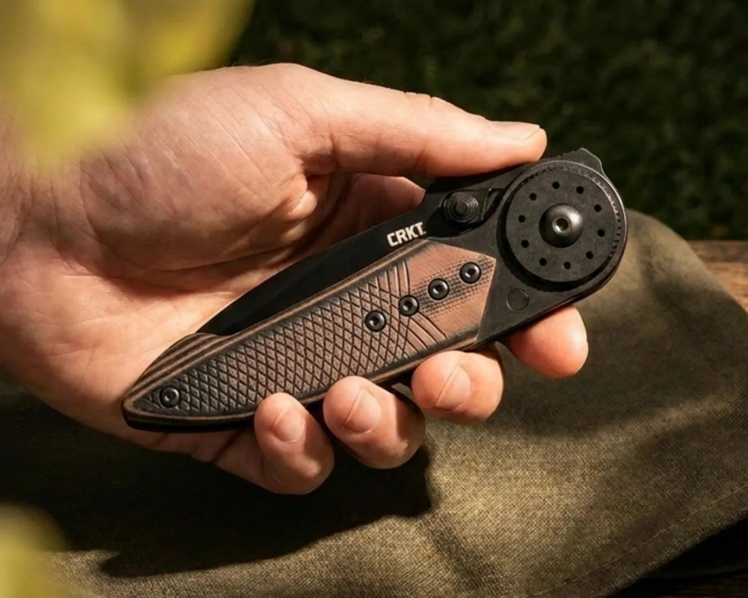 Hand holding a closed CRKT folding knife with textured brown and black handle.