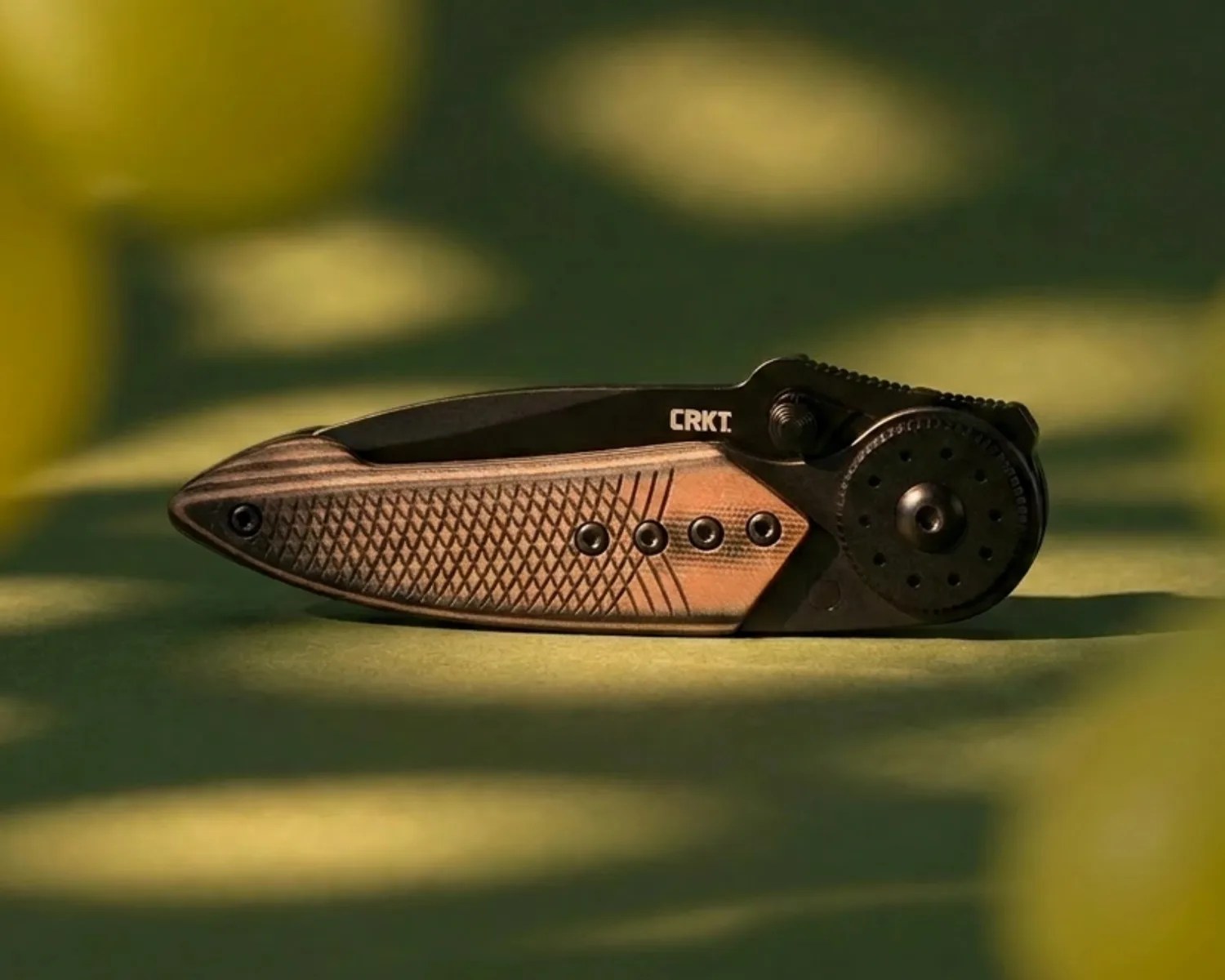 Closed CRKT folding knife with textured brown handle and black blade on green surface.