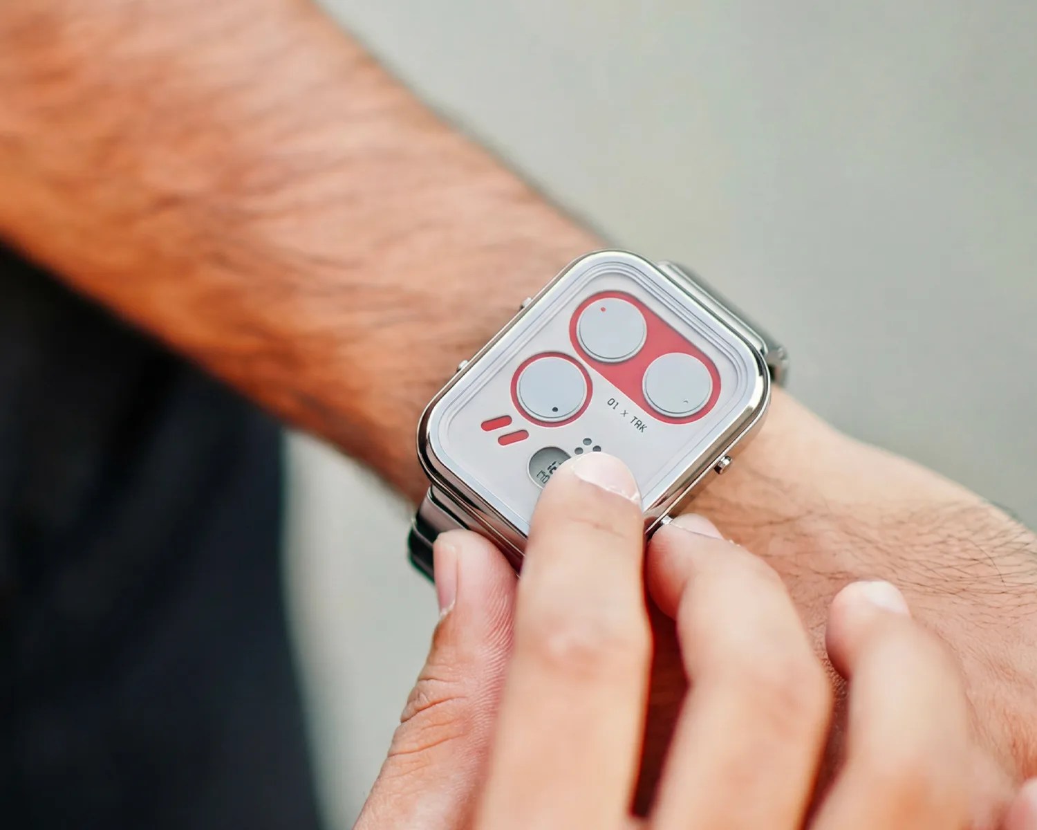Person wearing a silver watch with a white and red layout, finger touching the watch.