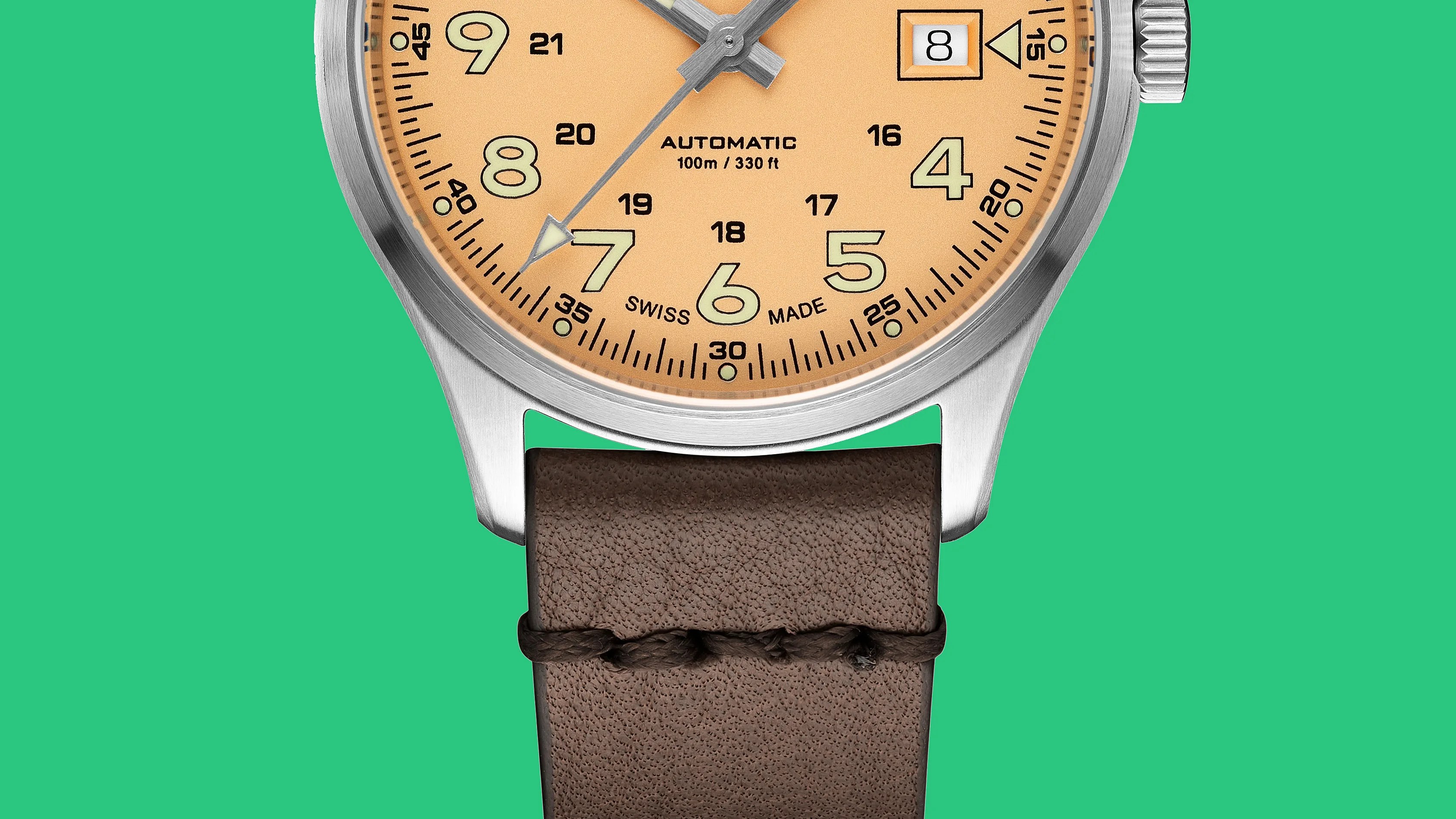 Close-up of a beige dial wristwatch with luminous numerals, date window, stainless steel case, and brown leather strap.